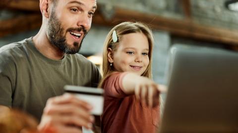 Father using credit card while shopping online with his daughter over a computer at home.