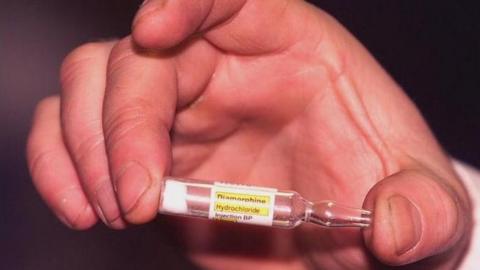 A hand is seen holding a phial of diamorphine hydrochloride, the medical name for heroin