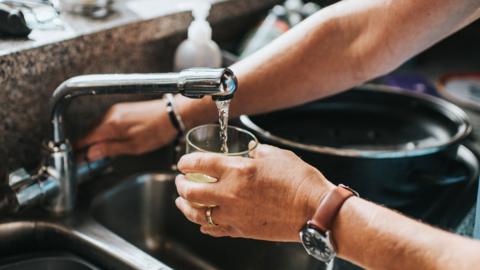 A person fills a glass from a kitchen tap