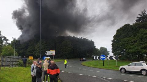 Black plumes of smoke with people watching from the road