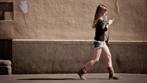 Street photography, woman walking while giving attention to her cell/mobile phone.