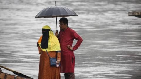 Bangladeshi passengers use an umbrella as they cross the Buriganga River by boat during a rainy day in Dhaka, Bangladesh