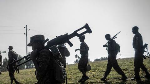 Photo of soldiers walking in a field carrying large weapons