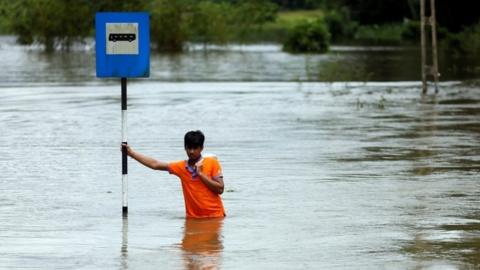 A man holds on to a bus stop on a flooded road in Sri Lanka