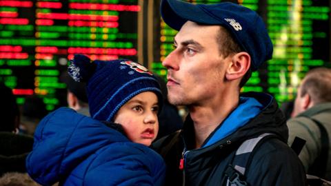 A man carries his child while waiting to board an evacuation train at Kyiv central train station on 28 February 2022