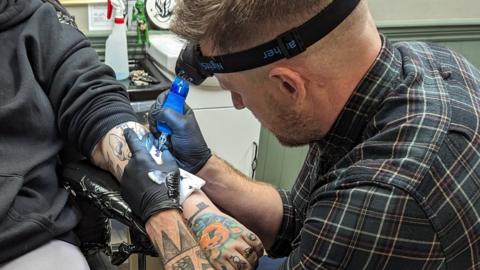 Liam Enisz tattooing a customer