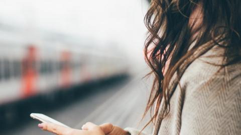 Woman waits for train with phone