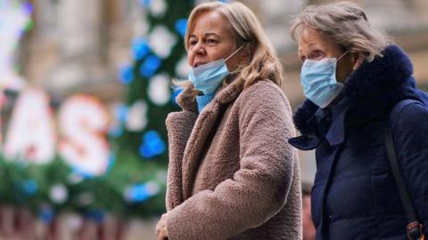 Two women wearing masks walk in Cardiff in front of a Merry Christmas sign