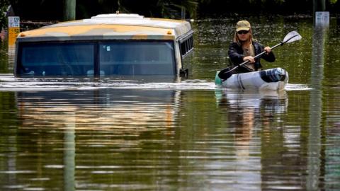 A man paddles his kayak next to a submerged bus on a flooded street in the town of Milton in suburban Brisbane on February 28, 2022.