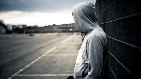 Teenager in hood leans on railing