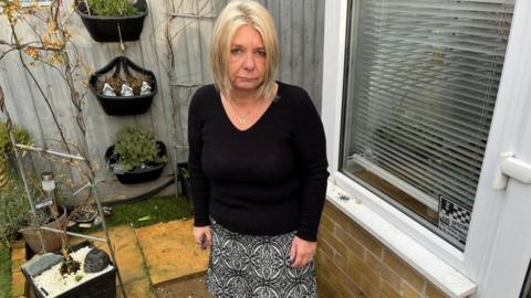 Woman with light-coloured hair standing on path in back garden