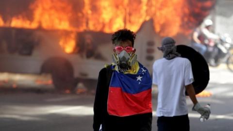 Opposition demonstrators stand in front of burning bus in Caracas
