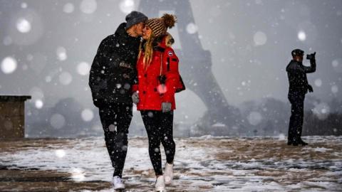 A couple is pictured in front of the Eiffel Tower as snow falls over Paris on 22 January 2019