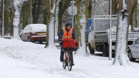 Postman wearing hi-viz cycles through snow