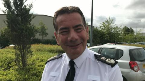 Man with short dark hair wearing police shirt and tie in a car park.