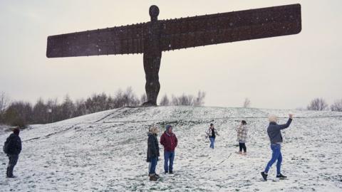 People play in snow around the Angel of the North