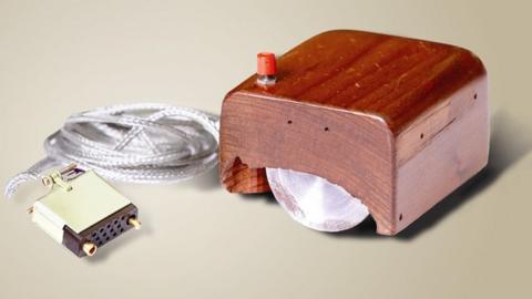 A wooden block with a visible steel wheel underneath, and one single red button, is seen with its cable