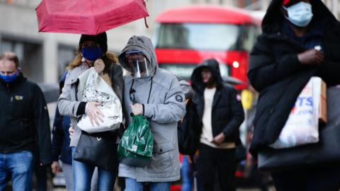 Shoppers wearing face masks, one also wearing a face shield, carry bags along Oxford Street in London