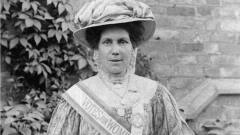 Alice Hawkins with a Votes for Women sash and poster