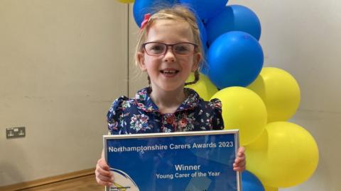 Young girl with glasses and hair in pony tails holds an award certificate