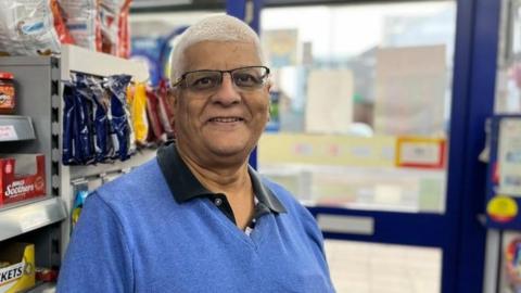 Man with short white hair and glasses in a small local shop