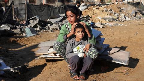 A Palestinian girl and her brother sit amidst the debris of a house following an Israeli strike in Rafah in the southern Gaza Strip - 18 November 2023