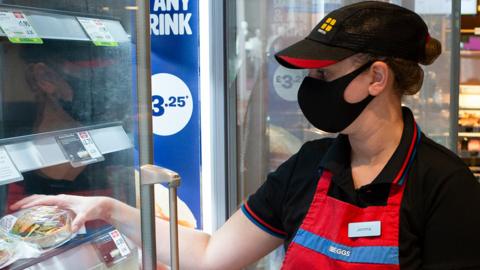 A member of staff adds food to the shelves in a Greggs bakery