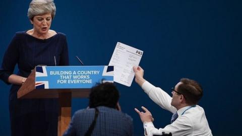 Comedian Simon Brodkin handing a piece of paper to the prime minister