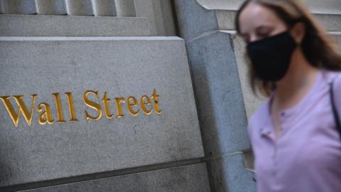 woman in mask walks by Wall Street sign