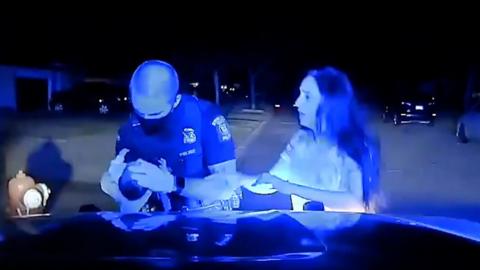 Michigan police officer examines the baby as the mother watches