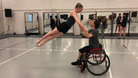 Joe Powell-Main lifts female ballet dancer from his wheelchair
