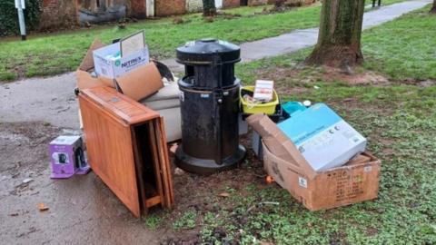 Folding table, washing up bowl and cardboard boxes dumped next to a bin on a public path