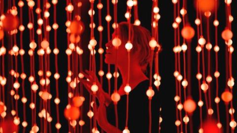 A woman stands among hundreds of suspended bright lights as part of an exhibition