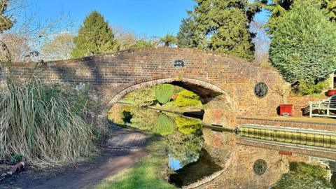 A brick bridge arches over a canal with sunny blue sky in the background