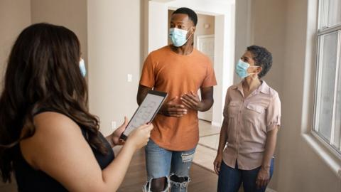 Stock image of an estate agent and a couple wearing face masks, on a house viewing