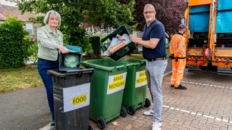 Two people load rubbish into bins