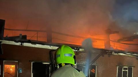 Firefighter tackling fire at a building behind Northern Waste Recycling