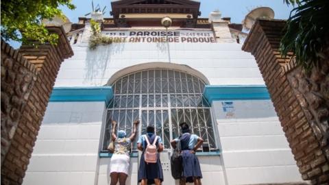 A woman and two youths people pray in front of the doors of the Saint Antoine church, where one of those kidnapped worked for decades, in Port-au-Prince, Haiti. Photo: 12 April 2021