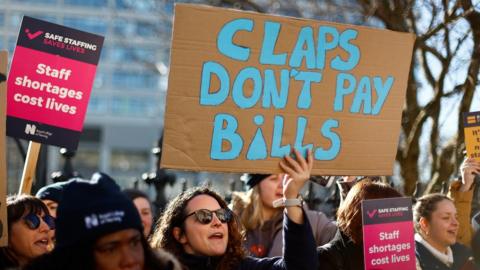 A woman holds a banner 'claps don't pay bills'