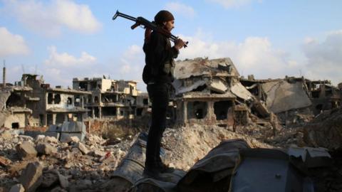 A rebel fighter stands amid the rubble of destroyed buildings in a rebel-held area of Deraa, in southern Syria, on 14 March 2017