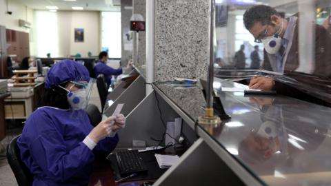 A bank employee wear protective masks in Tehran, Iran (17 March 2020)