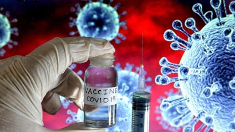 A syringe and a gloved hand holding a vial labelled "VACCINE COVID-19" with a background graphic illustration of a virus