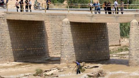 A picture obtained by AFP from the Iranian news agency Tasnim on July 23, 2022, shows people standing on a bridge above a river, after flooding caused by heavy rainfall in southern Iran's Estahban county