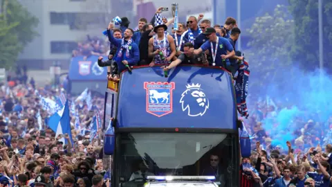 Ipswich Town players celebrate on a bus, with thousands of fans nearby