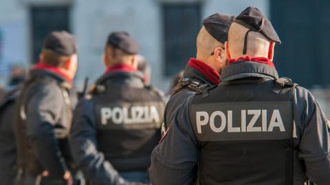 Police stand in a public place, their 'polizia' signs visible.