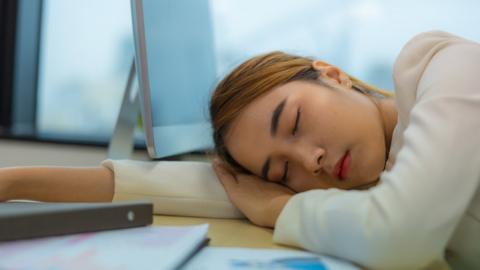 A stock image of a young woman sleeping at her desk