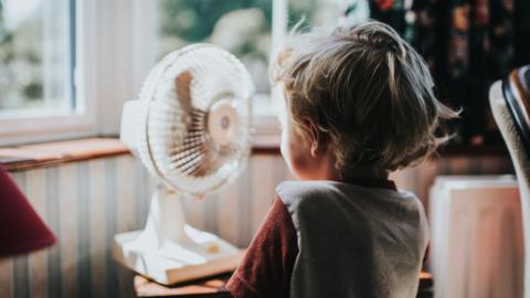 A little boy stands in front of a fan