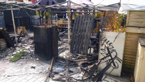 A scene of fire damage with burnt picnic tables and damaged gazebos at Mourne Seafood