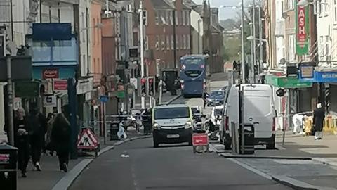 Shopping street showing police tape, police van and bus