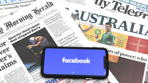 A phone showing the Facebook logo on a spread of Australian newspapers